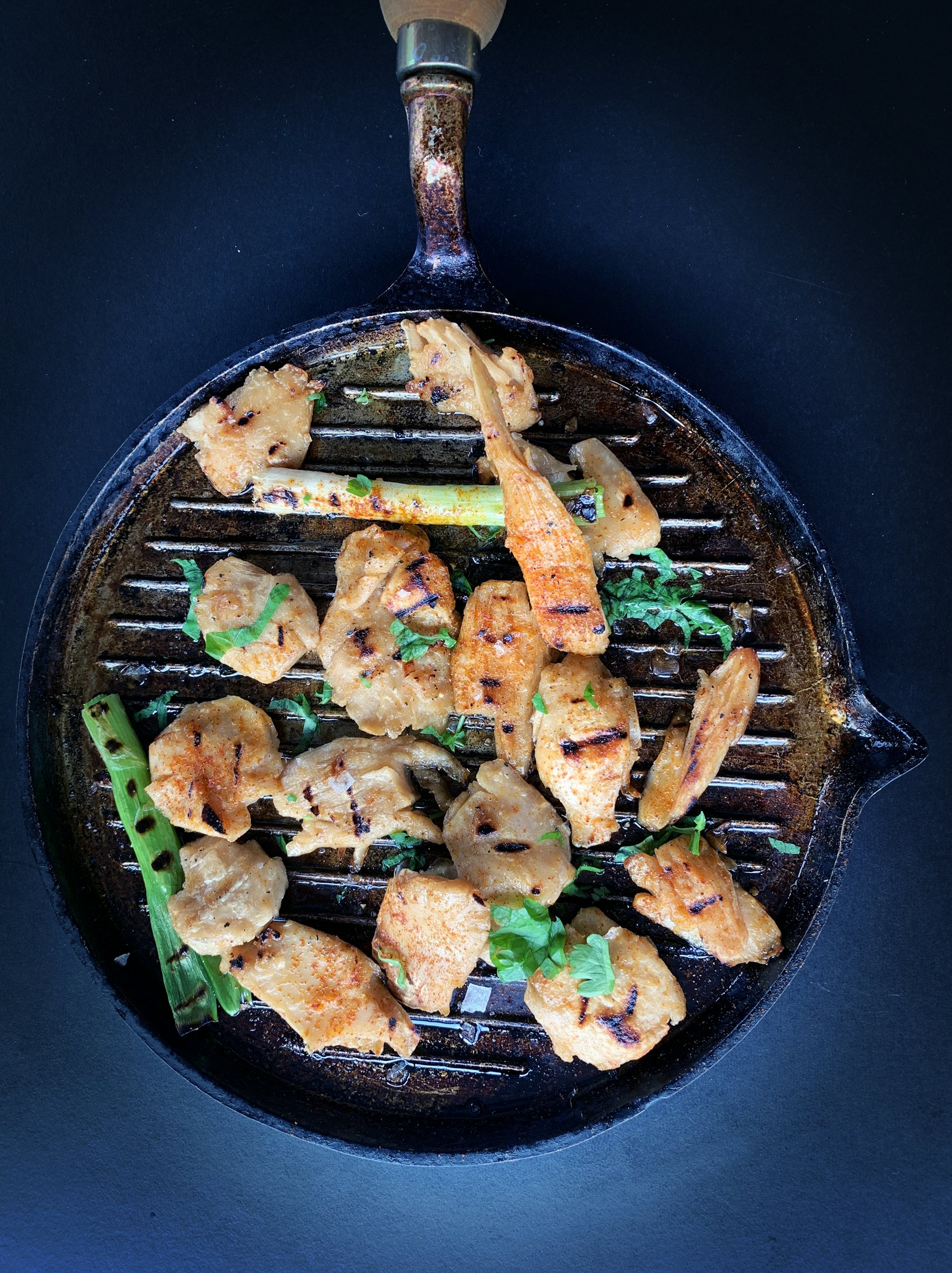 Seasoned chicken and charred scallions on a ridged grill pan, shot from above