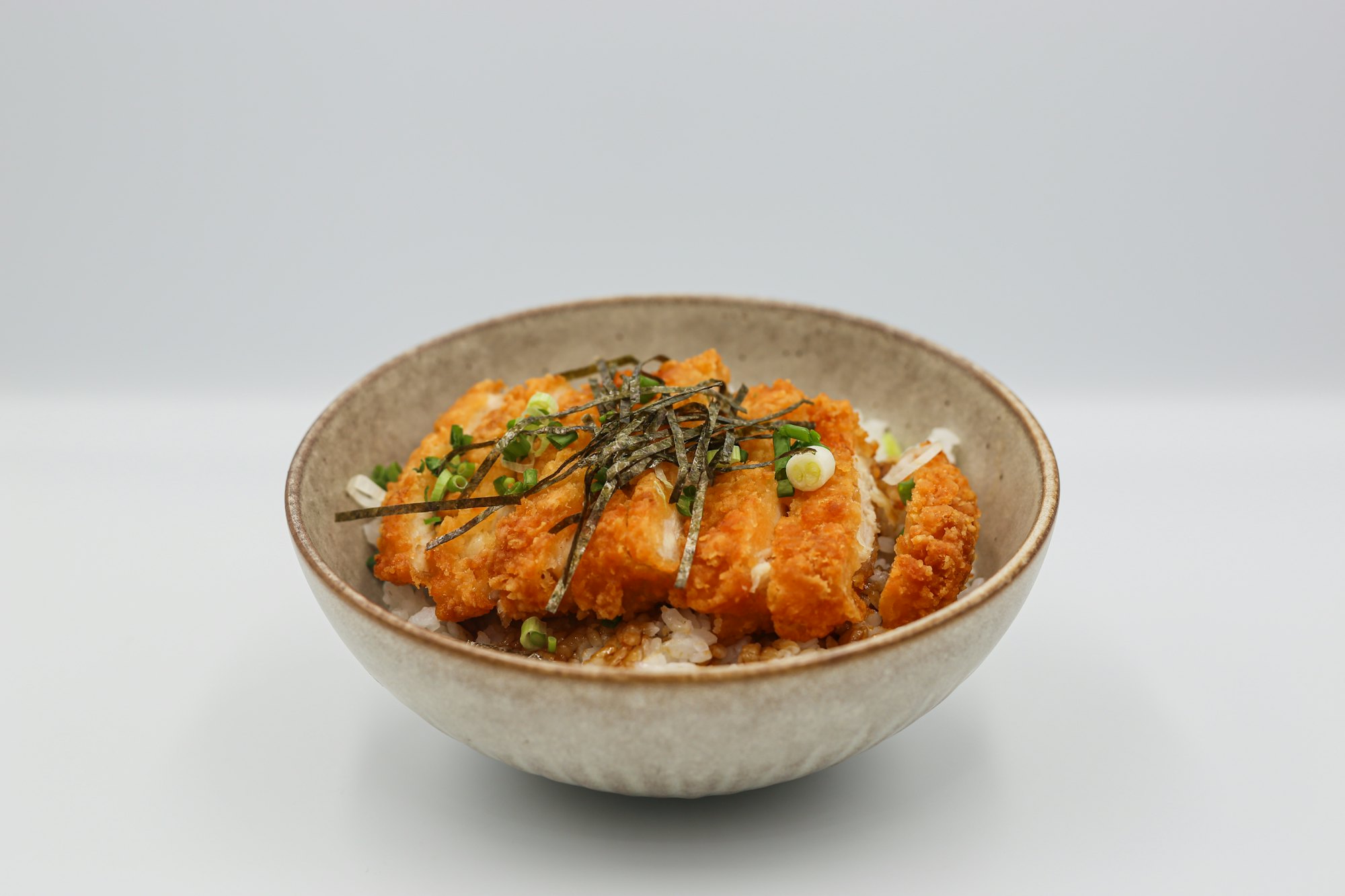 A chicken and rice bowl under a spoonful of sauce, shot from above on a dark table